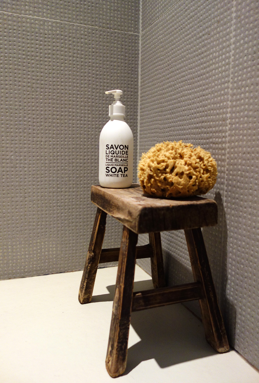 C'est grâce au tabouret ancien en orme que la douche devient confortable. On peut y poser une belle éponge naturelle et le savon Thé Blanc de Compagnie de Provence